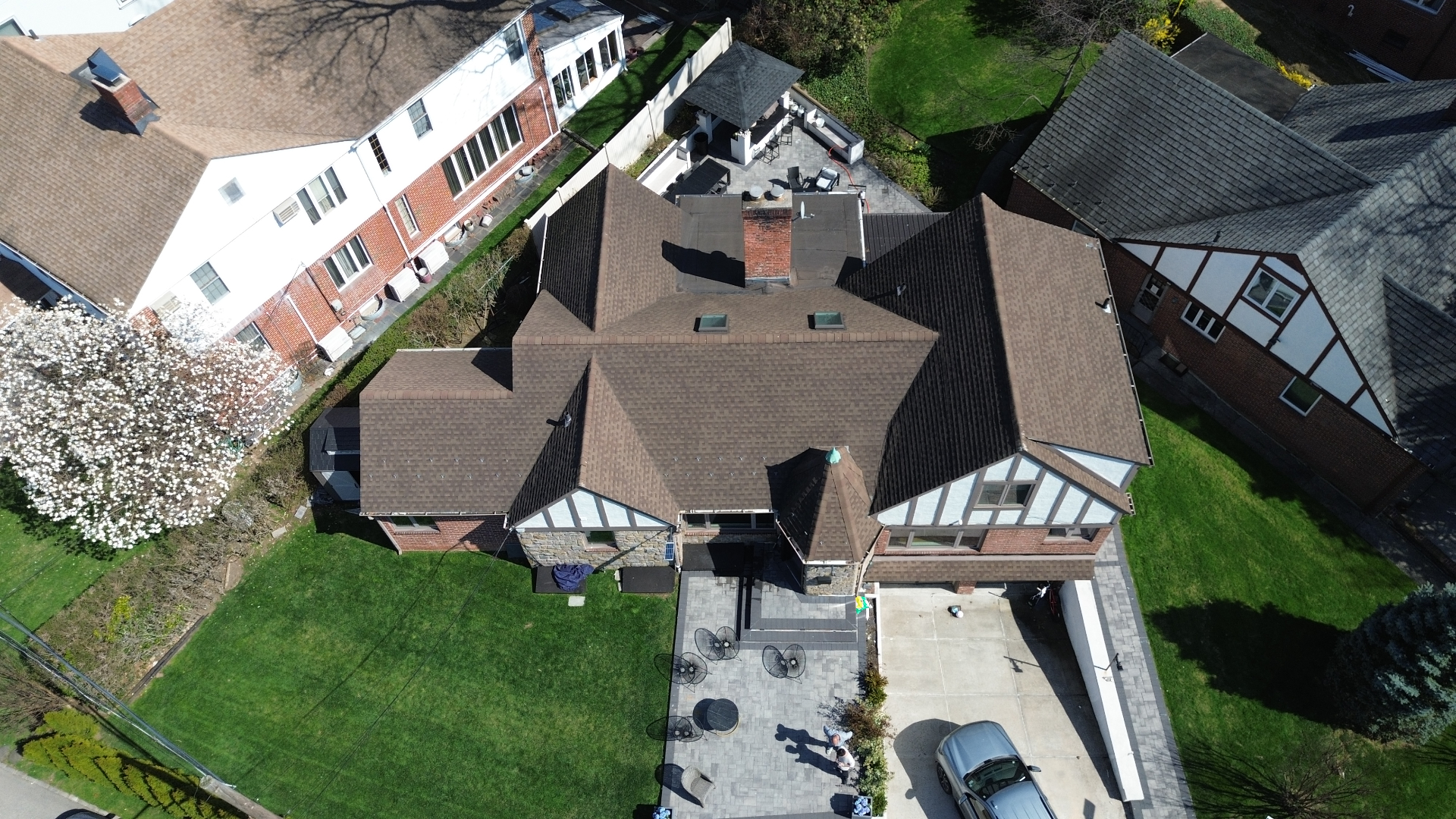 Top-down drone view of a freshly completed brown shingle roof with multiple peaks and gables in Queens